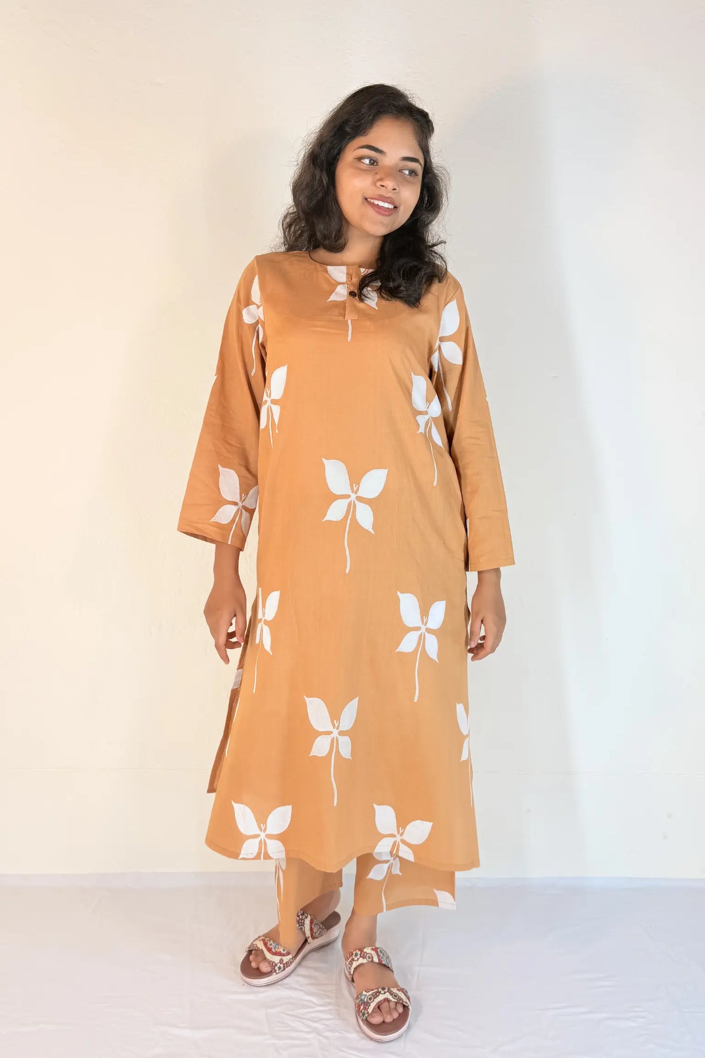 Woman wearing a mustard yellow dress with white floral patterns on a plain background