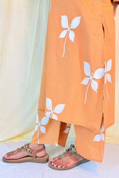 Orange pants with white floral patterns worn by a person, standing against a light background.