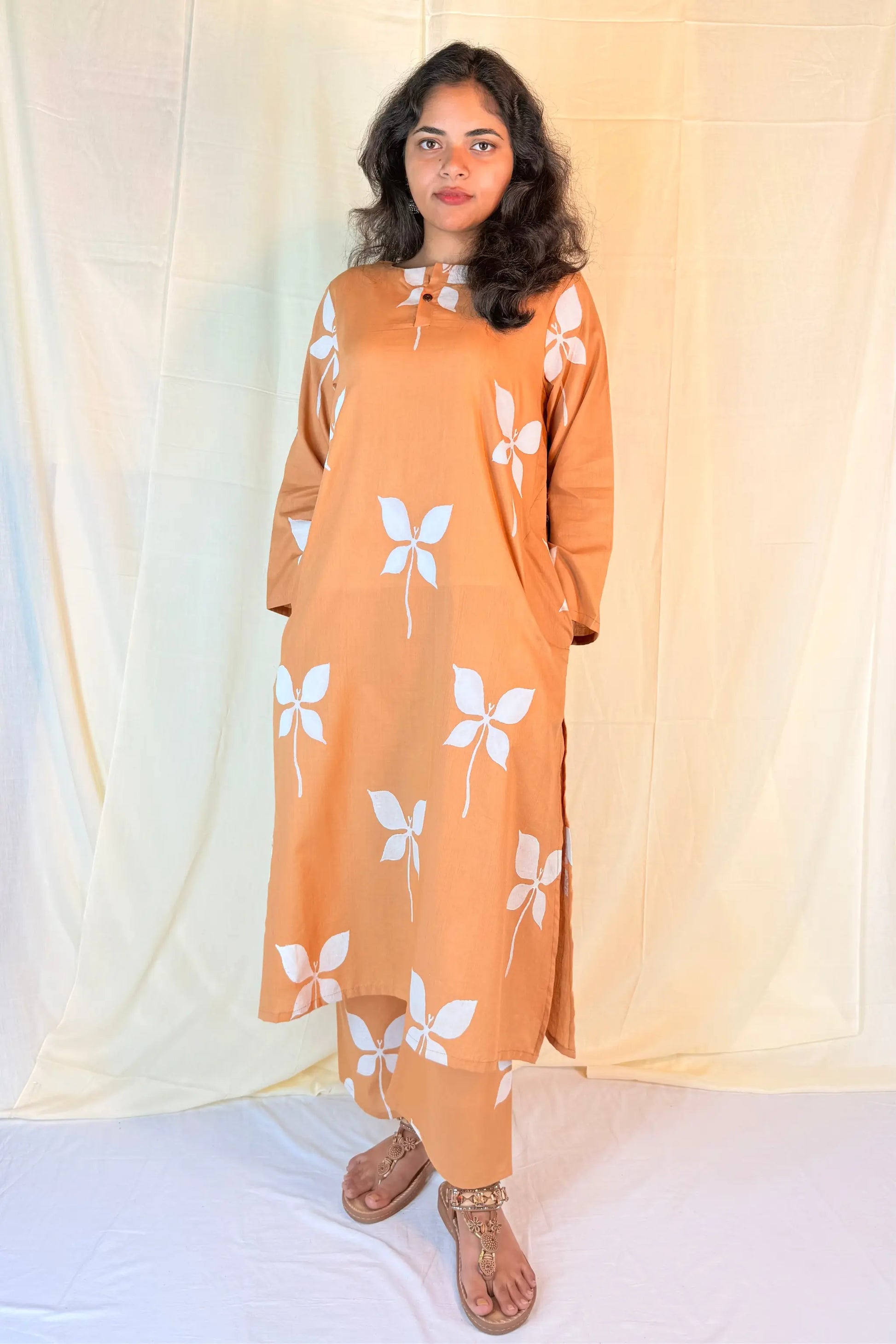 Woman wearing a mustard yellow dress with white floral patterns against a light curtain background