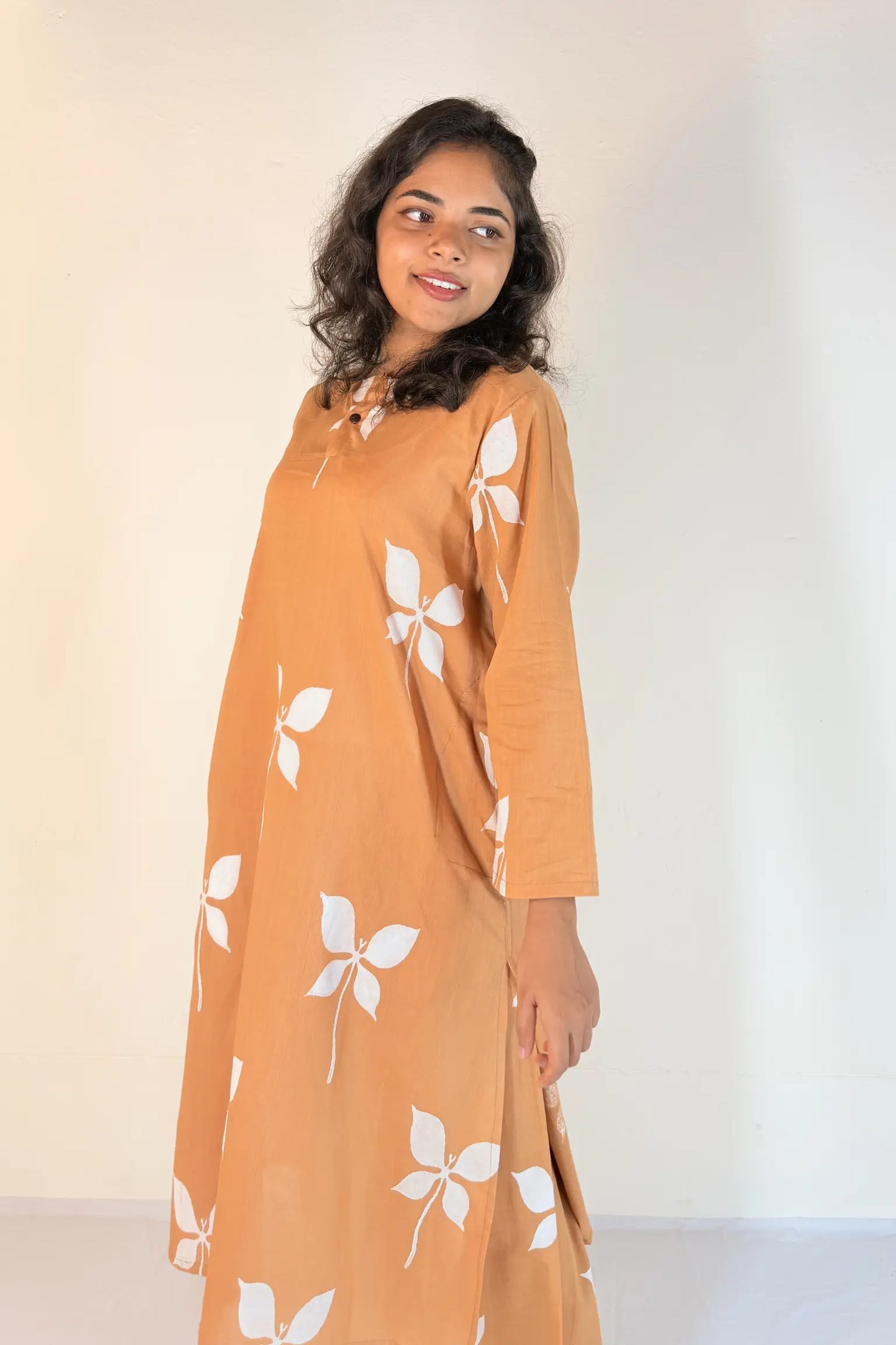 Woman wearing a mustard yellow dress with white floral patterns against a plain background