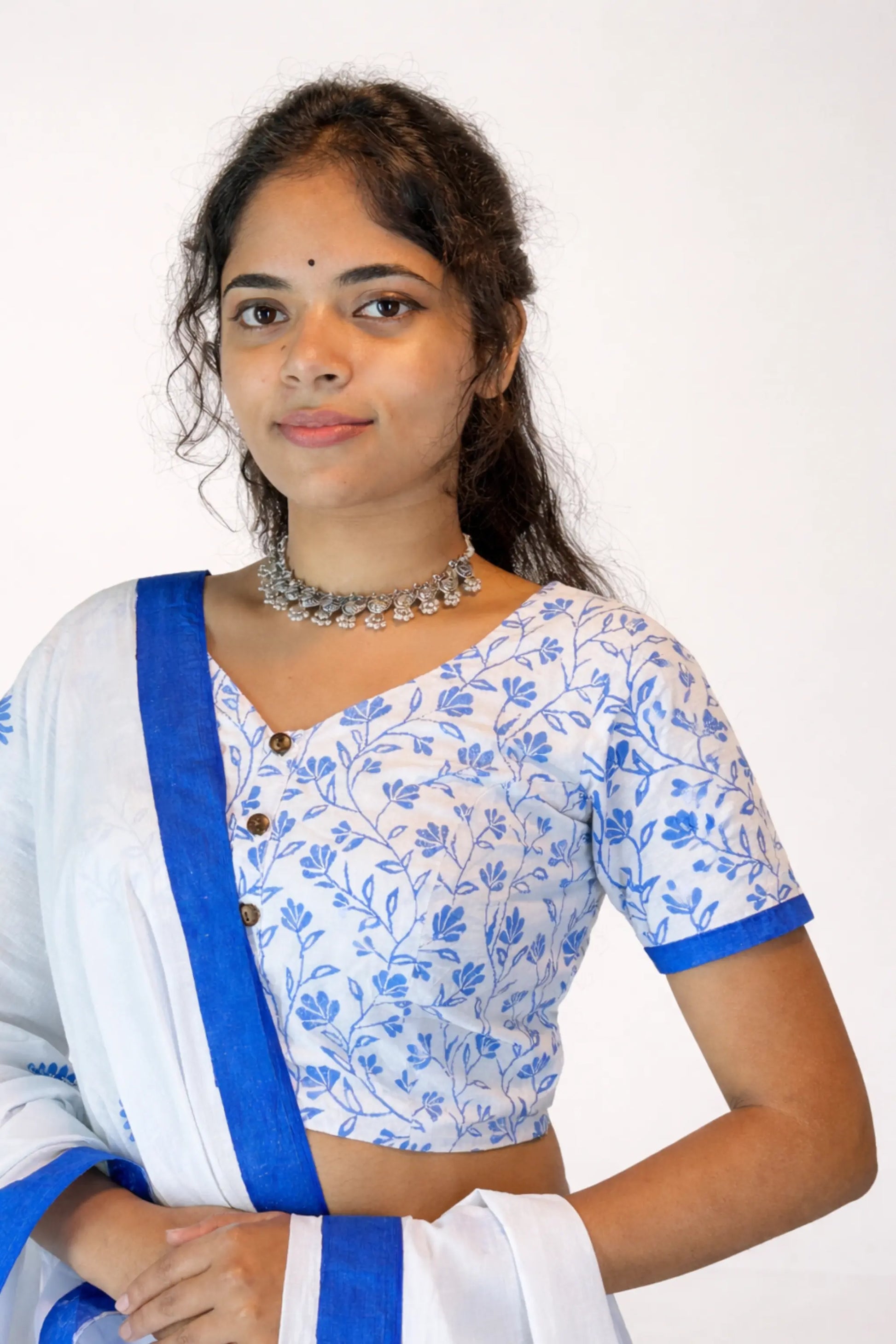 Portrait of a woman wearing a blue and white hand block printed cotton gopi dress blouse with floral patterns, paired with a white dupatta with blue border, accessorized with silver jewelry against a clean studio background.