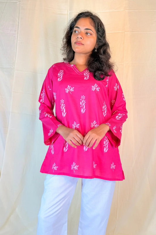 Woman wearing a pink patterned top and white pants against a beige background