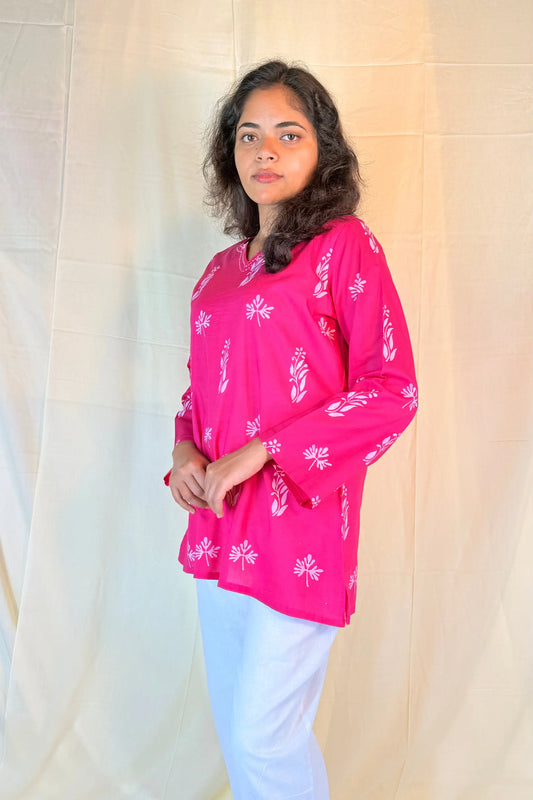Woman wearing a bright pink top with white floral patterns against a neutral background