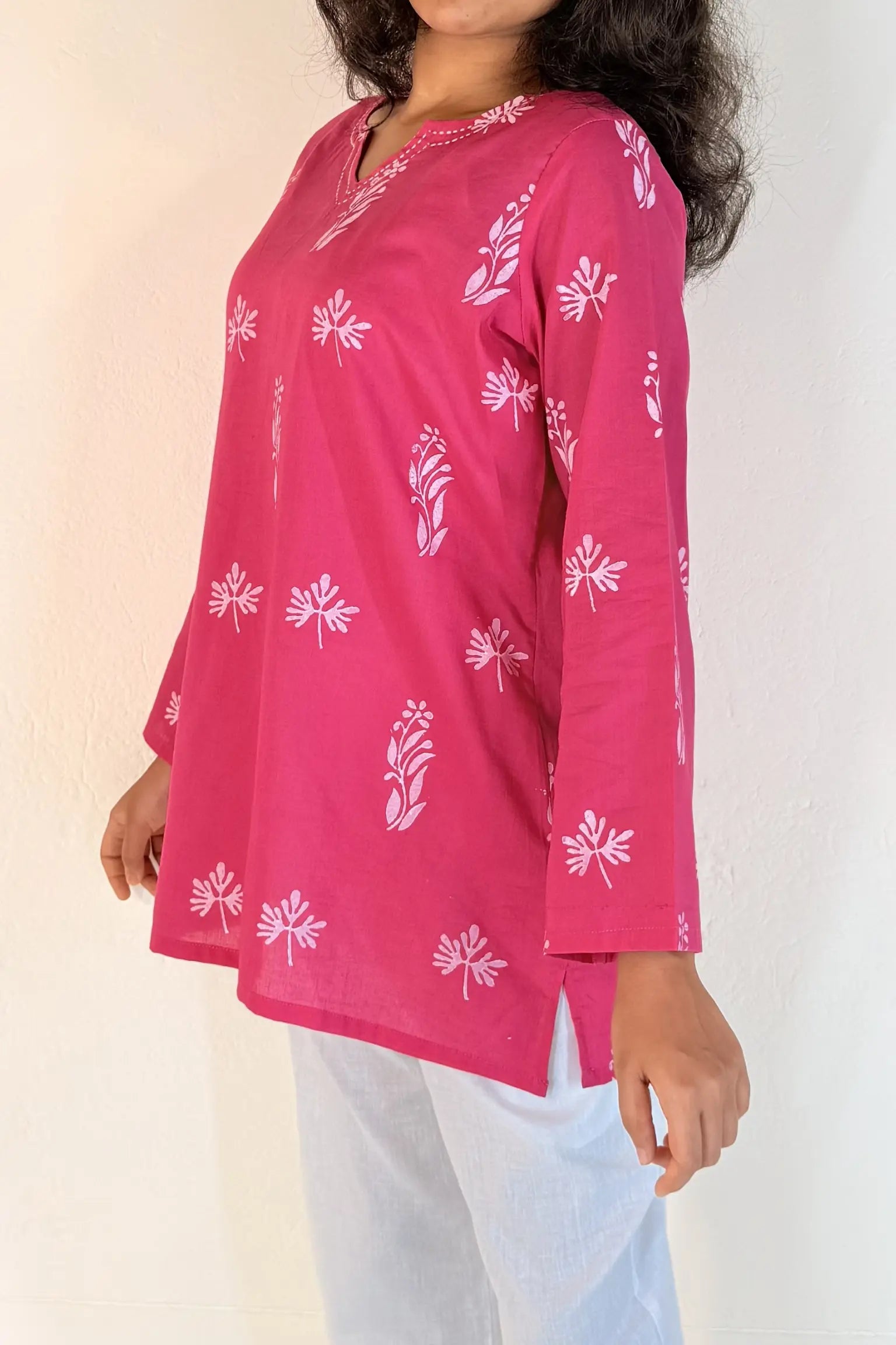 Person wearing a pink traditional top with white floral patterns on a plain background
