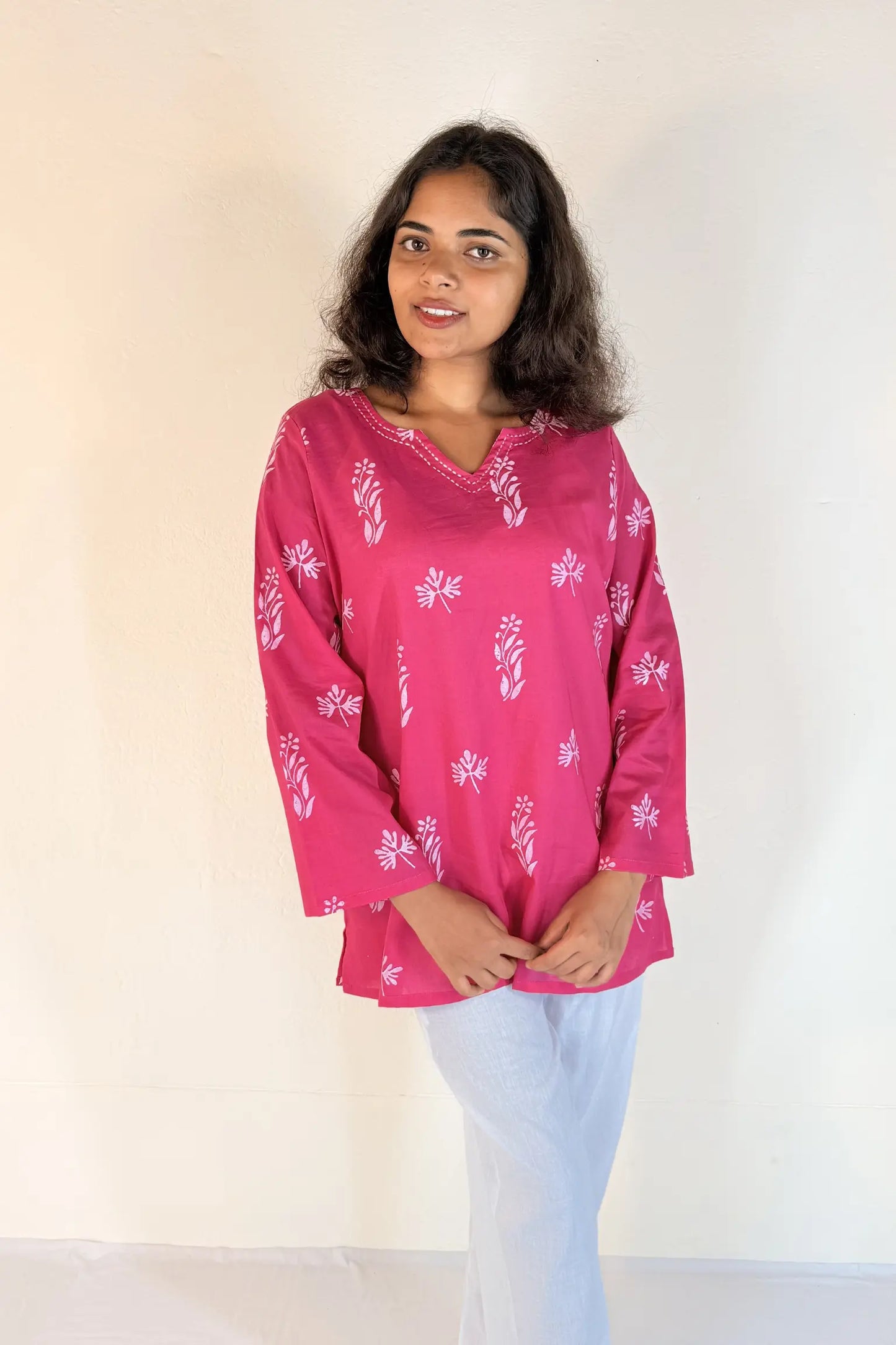 Woman wearing a pink blouse with white patterns against a plain background