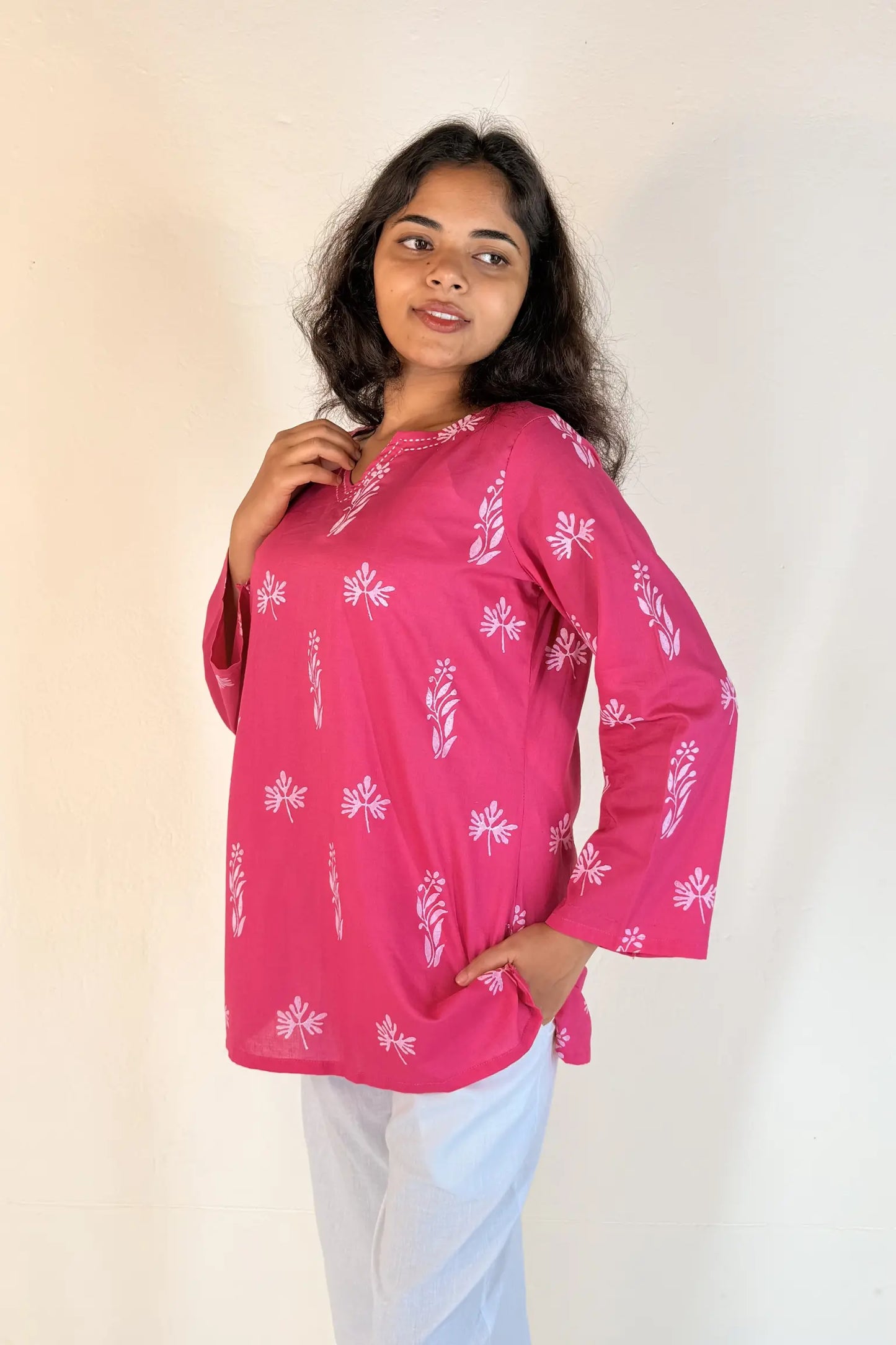 Woman wearing a pink blouse with white patterns against a plain background