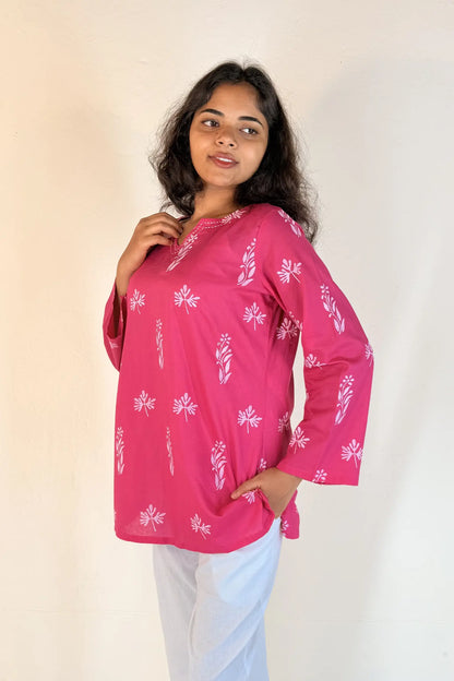Woman wearing a pink blouse with white patterns against a plain background