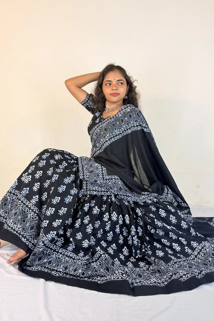 Woman wearing a black and white patterned Gopi Dress sitting on a white bed.
