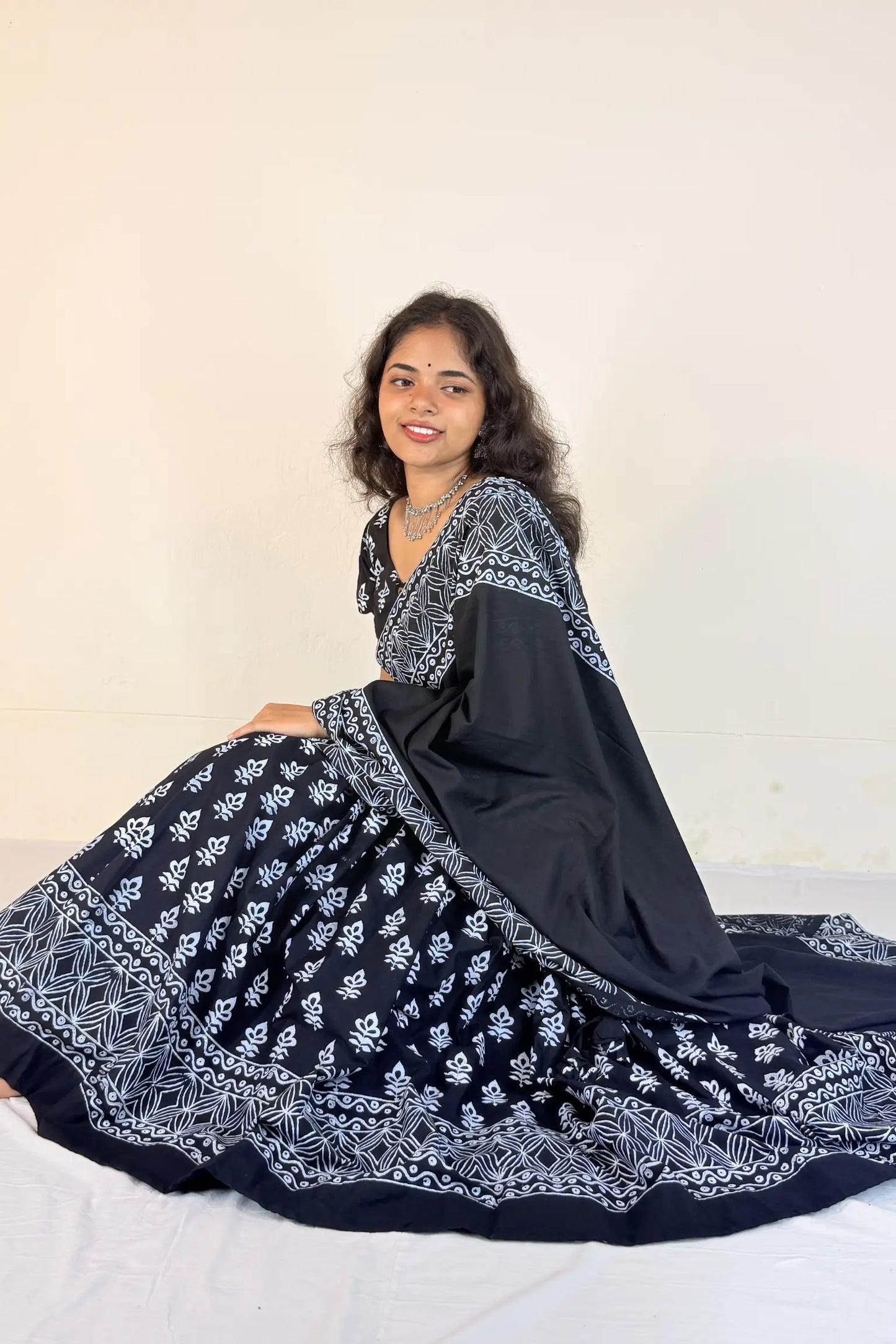 Woman wearing a colorful traditional outfit with a black blouse, black and white gopi dress, and floral hair accessory.