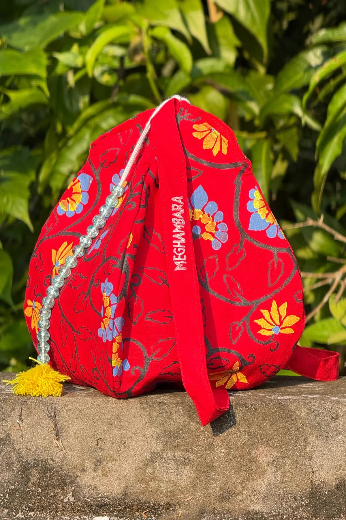 Handcrafted red japa mala bag with colorful floral block print, bead string and tassel detail, made by Meghambara