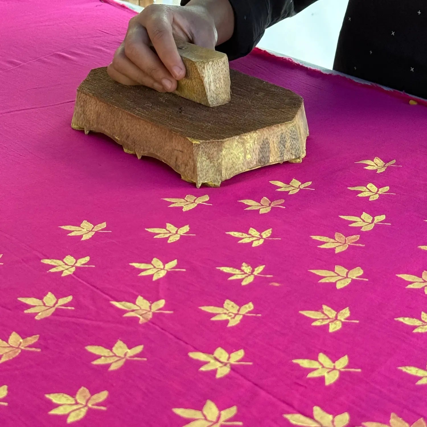 Person stamping a pink fabric with yellow floral patterns using a wooden block.