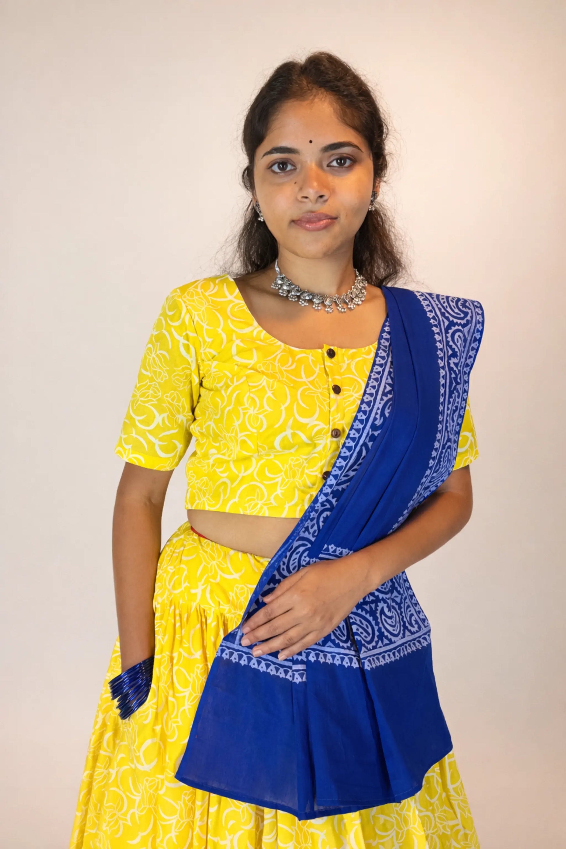 Woman wearing a yellow and blue traditional outfit with a plain background