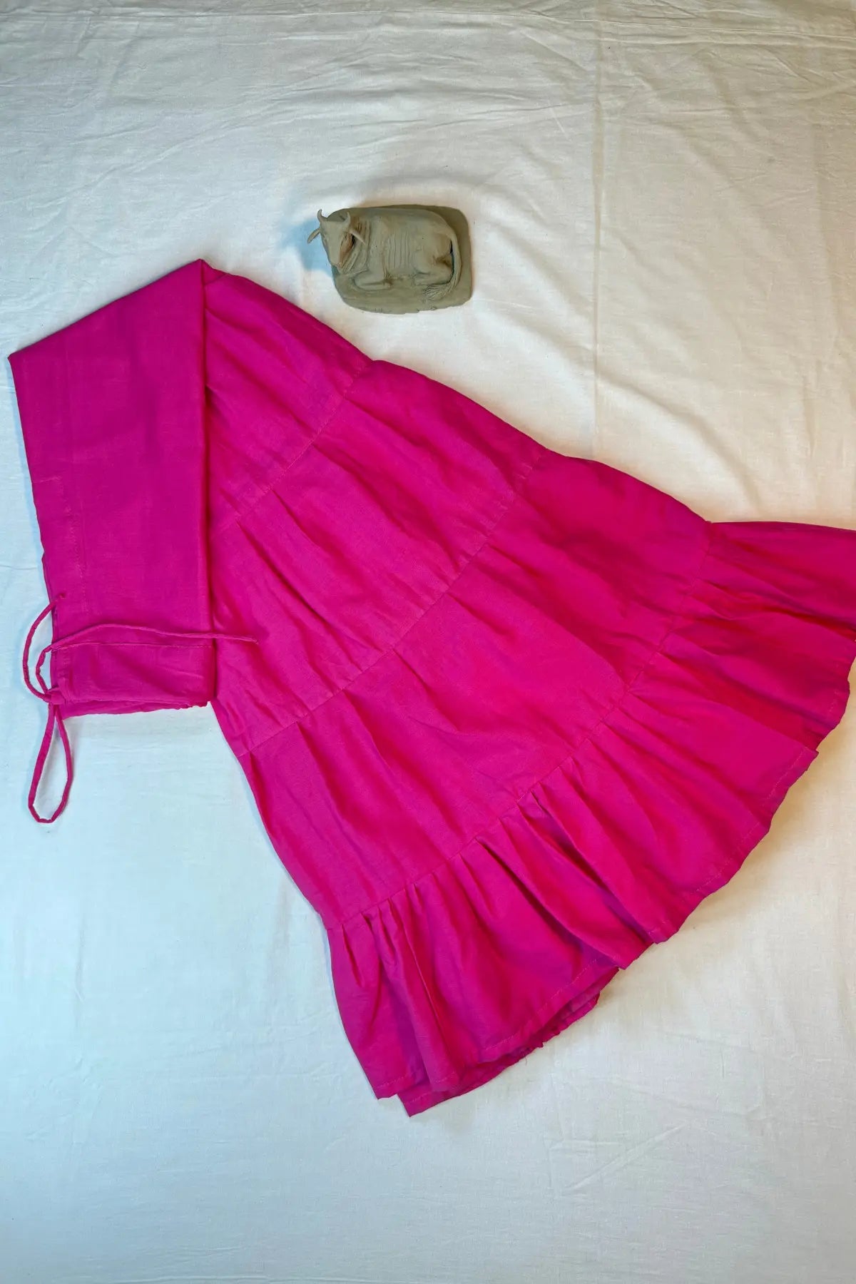 Flat lay of bright pink cotton petticoat underskirt with adjustable waist tie, showcasing tiered panels and breathable fabric.