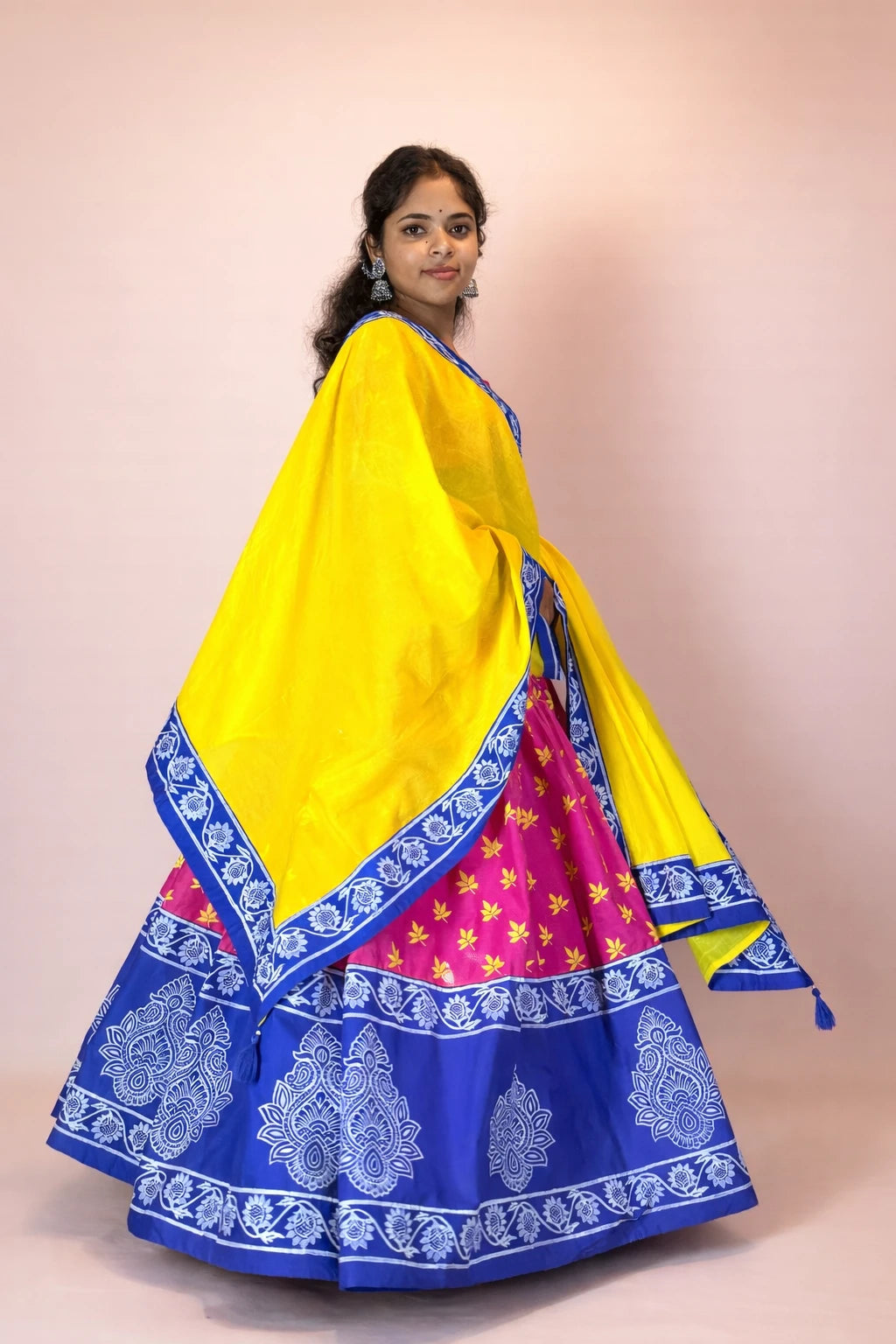 Woman wearing a traditional outfit with a yellow dupatta and blue and pink skirt on a beige background