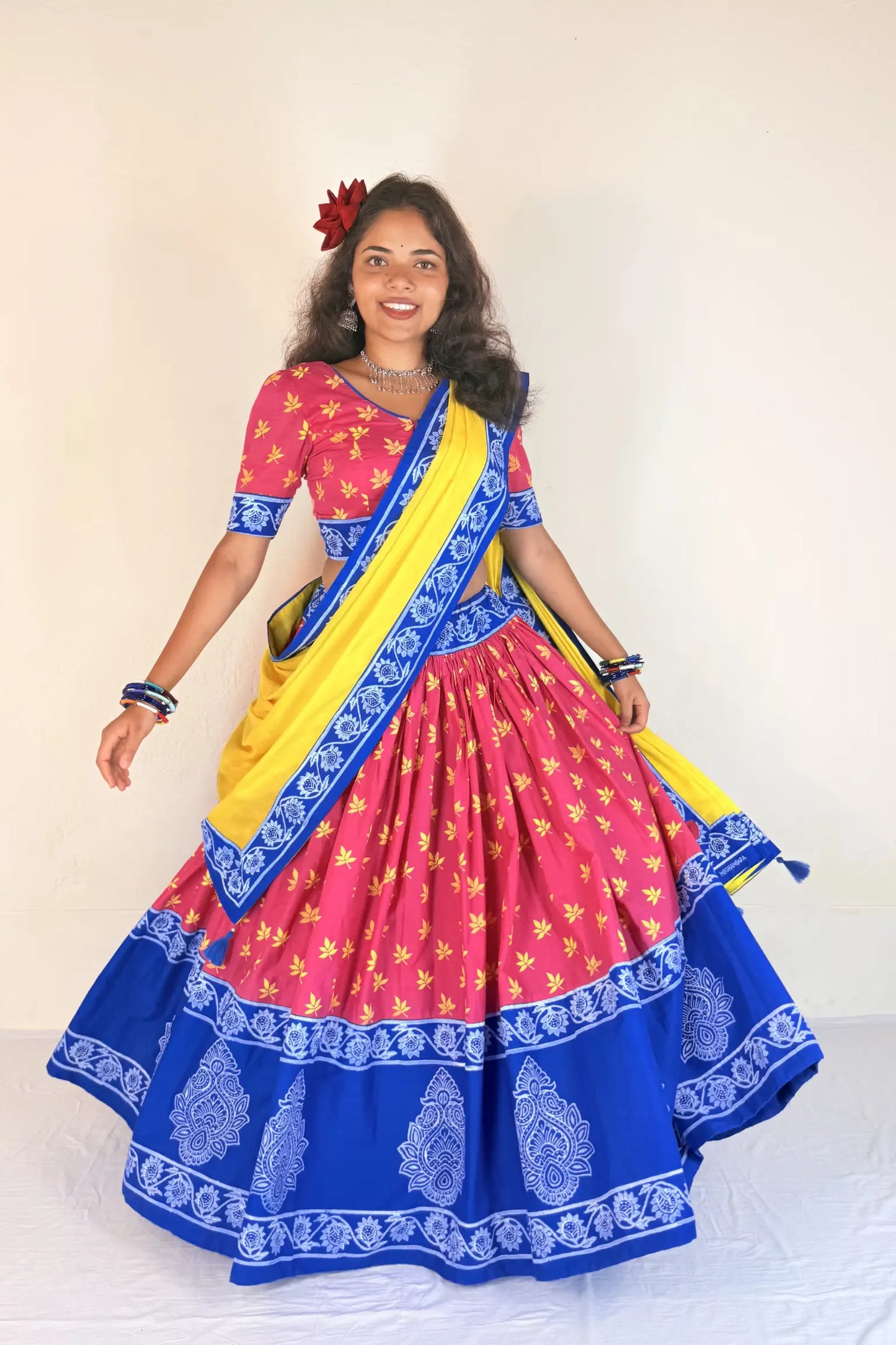 Woman wearing a colorful traditional outfit with a pink blouse, blue Gopi Dress, and yellow sari.