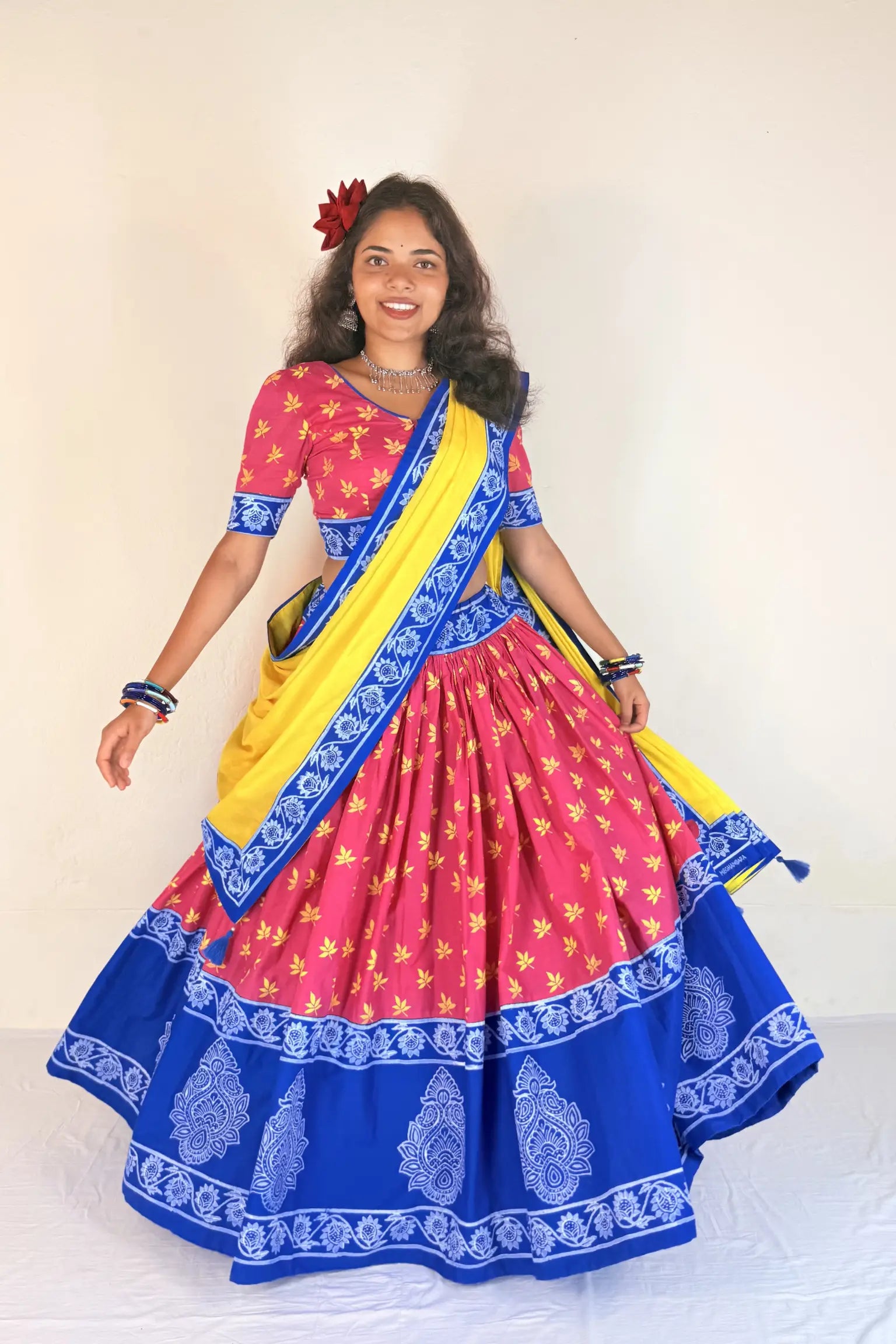 Woman wearing a colorful traditional outfit with a pink blouse, blue Gopi Dress, and yellow sari.