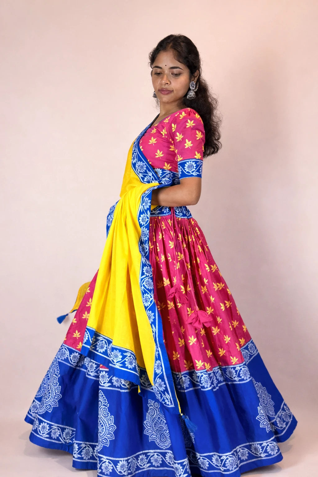 Angled side pose of Rasika Rangini hand block printed Gopi dress highlighting yellow dupatta and pink skirt with blue border