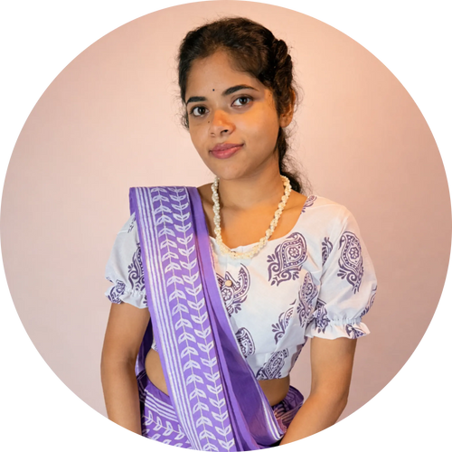 Woman wearing a white blouse with purple patterns and a matching purple gopi skirt set against a pink background